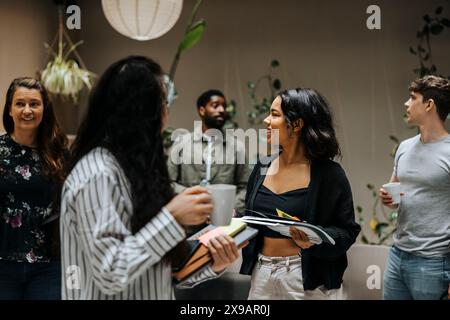 Smiling female business professionals holding documents with colleagues while standing at office Stock Photo