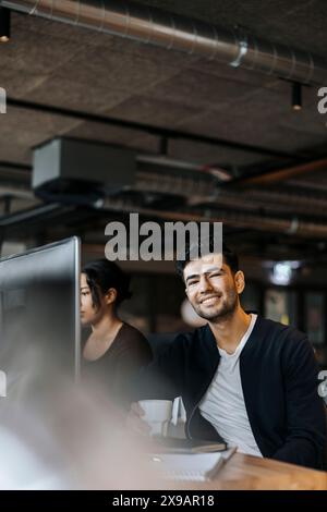 Smiling young male programmer next to female colleague at tech startup office Stock Photo