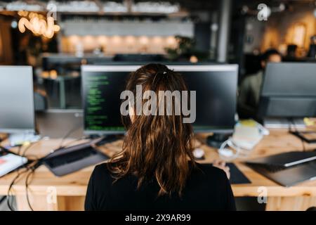 Rear of female coder with ponytail sitting at desk in office Stock Photo