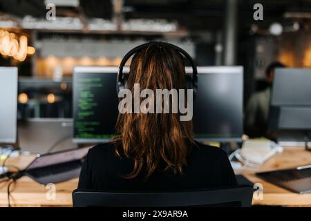 Rear view of female coder with headphones working on computer at office Stock Photo