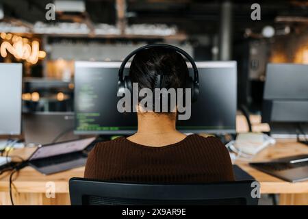Rear view of female computer programmer with headphones doing coding at tech start up at office Stock Photo