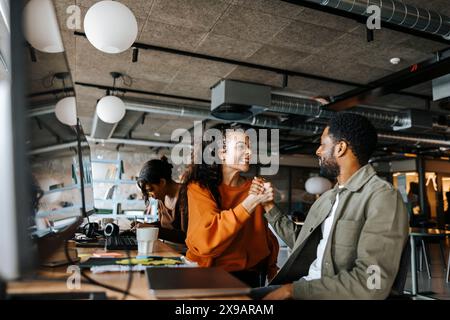 Excited male and female entrepreneurs celebrating achievement sitting at desk in office Stock Photo