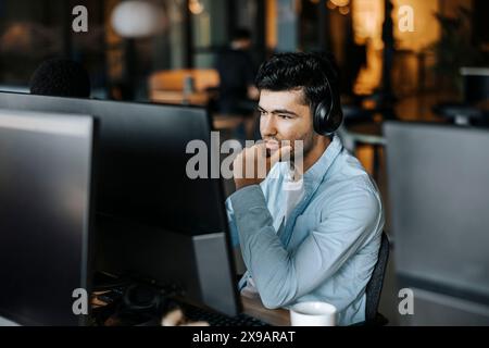 Thoughtful male entrepreneur with hand on chin sitting and looking at computer in office Stock Photo