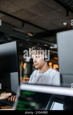 Young male programmer doing coding on computer while sitting at tech start up office Stock Photo
