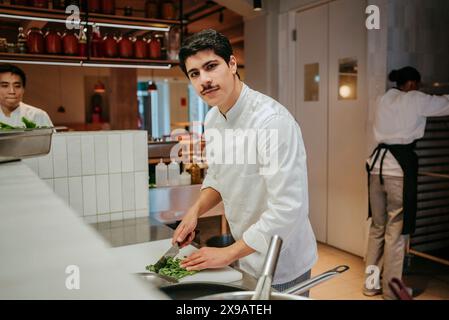 Portrait of male chef cutting broccolini while standing with coworkers in commercial kitchen Stock Photo
