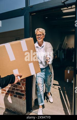 Happy female owner taking cardboard box from colleague at clothing store Stock Photo