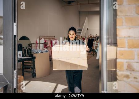 Female owner carrying cardboard box walking towards door in clothing store Stock Photo