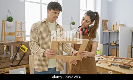 A man and woman work together as a team in a carpentry workshop, carefully examining a wooden frame. Stock Photo
