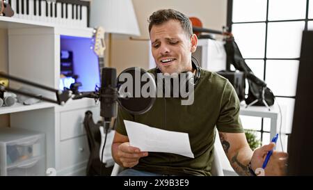 A hispanic man sings indoors while recording in a professional music studio, with a microphone and headphones. Stock Photo