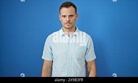 Handsome young man with a beard posing in front of a blue wall, exuding confidence and style. Stock Photo