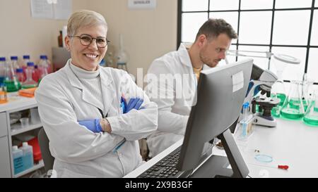 Smiling woman and focused man, both scientists, working together indoors in a modern laboratory. Stock Photo