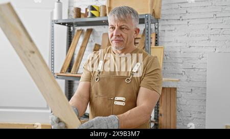 Middle-aged man in workshop examining wooden plank, showcasing mature carpentry skills in an indoor setting. Stock Photo