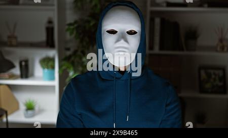 A mysterious person in a mask posing with a hooded sweatshirt in a blurred office setting Stock Photo