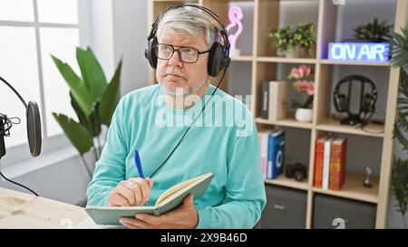 Mature man with headphones in radio studio taking notes while broadcasting. Stock Photo