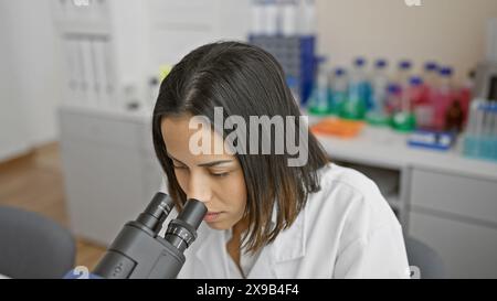 Concentrated young woman scientist using microscope in a modern laboratory setting. Stock Photo