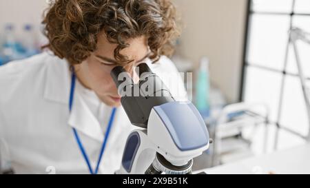 Young hispanic male scientist examining samples with a microscope in a bright laboratory setting. Stock Photo