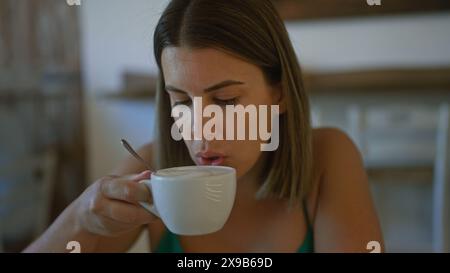 Young hispanic woman sipping coffee in an italian cafeteria, capturing a serene indoor moment. Stock Photo