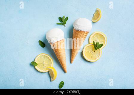 Scoop of lemon ice cream in wafer cone and lemon slices on light blue background, top view. Trendy creative layout. Stock Photo