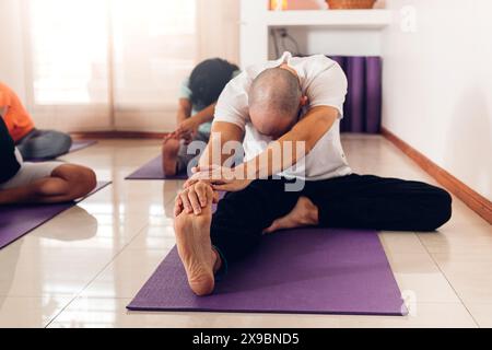 Young man in class in class doing the yoga Janu Sirsasana pose: The Head to Knee Stock Photo