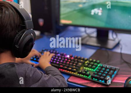 child with back headphones playing video games on a computer with a keyboard with lights. Stock Photo