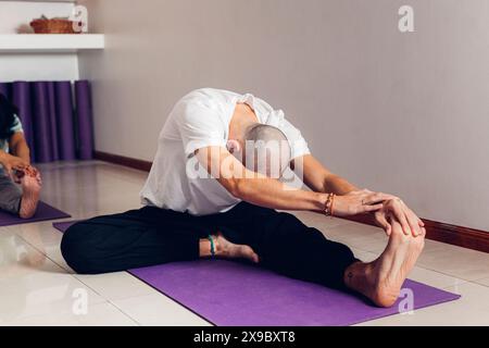 Young man in class in class doing the yoga Janu Sirsasana pose: The Head to Knee Stock Photo