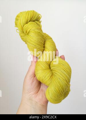 Close-up photo of a twisted yellow-green hand dyed thin yarn skein in a woman's hand on a white background Stock Photo