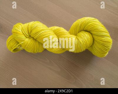 Table top photo of one twisted yellow-green hand dyed thin yarn skein on a wooden background Stock Photo