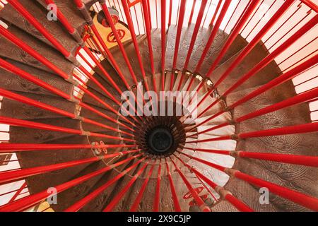 a spiral staircase inside Ljubljana Castle, leading up to one of the towers. A bright red bannister connects to intricately patterned wooden steps Stock Photo