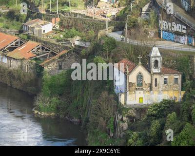 Small chapel and surrounding buildings on an overgrown, rocky cliff by a river with graffiti on walls, spring in the old town of Porto on the Douro Stock Photo