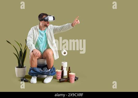 Young man using VR glasses on toilet bowl against green background Stock Photo