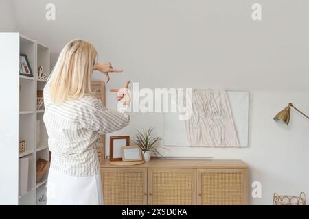 Mature woman looking at hanging 3D painting on light wall in living room, back view Stock Photo