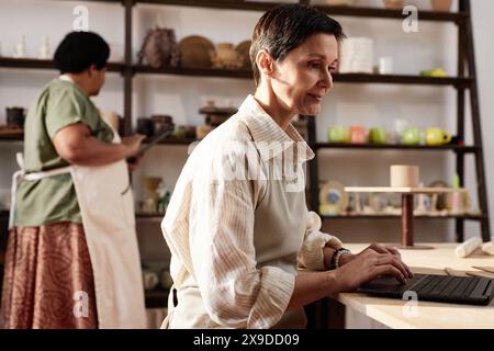 Side view portrait of mature woman using computer in art studio and managing small business copy space Stock Photo