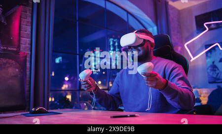 Stylish Man Using Virtual Reality Headset with Controllers at Home in Loft Apartment. Young African American Male Surfing the Web, Spending Time in VR Digital Office. POV from Screen Perspective. Stock Photo