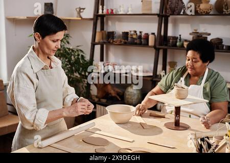 High angle view at two senior women enjoying pottery class in art studio lit by sunlight copy space Stock Photo
