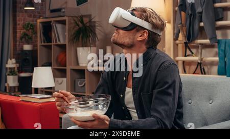 Television Sitcom Concept: Guy Using Virtual Reality Headset Eating Breakfast in Living Room. Funny Sketch About Internet Addiction. Comedy Series Broadcast Network Channel, Streaming Service. Stock Photo