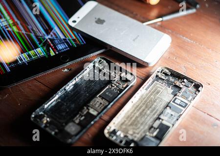 A disassembled smartphone with its internal components exposed, placed on a wooden surface. Nearby, a damaged tablet with a colorful striped screen an Stock Photo