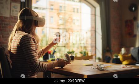 Blonde Woman Wearing 3D VR Headset And Using Modern Controllers Indoors. Female Designer Working in Futuristic Application. New Technologies and Augmented Reality Concept. Stock Photo
