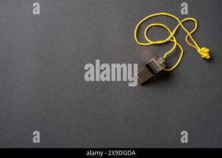 Top view of metal whistle with yellow string on dark gray background Stock Photo