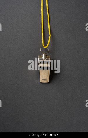 Top view of metal whistle with yellow string on dark gray background Stock Photo