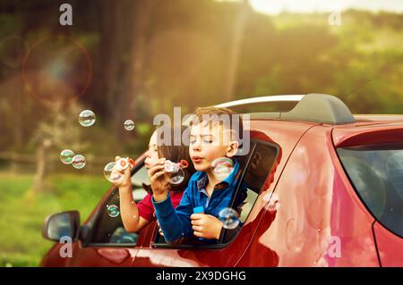 Blowing, bubbles and children for fun in countryside by window, outdoor or nature with soap toys. Kids, boy and girl in car for playing, freedom and Stock Photo