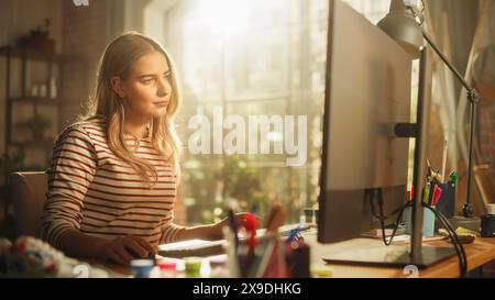 Smiling Female Teen Working on her Personal Computer. Sitting Behind the Desk in Loft Sunny Room. Freelancer Working From Home. Creative Woman Checking Social Media and Browsing Internet. Stock Photo