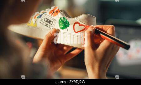 Close Up Over the Shoulder View of Teen Female Artist Applying Colourful Brave Design on Sneakers, Spending Time at Home. Girl Using Computer with 3D Model of Footwear. Drawing on Shoes Concept. Stock Photo