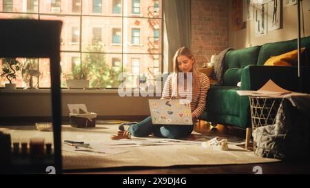 Woman Using Laptop at Home, Does Remote Work. Smiling Female Sitting on the Floor, Working with Papers, Documents, Brainstorming Creative Project with Research. Productivity in Sunny Living Room. Stock Photo