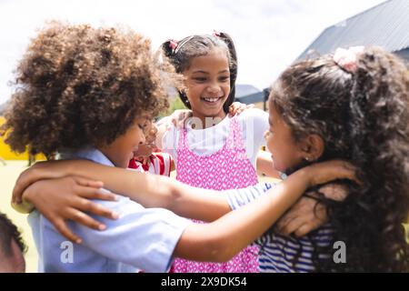 In school, diverse group of young students hugging, laughing outside Stock Photo