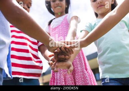 In school outside, diverse group of young students are joining hands Stock Photo