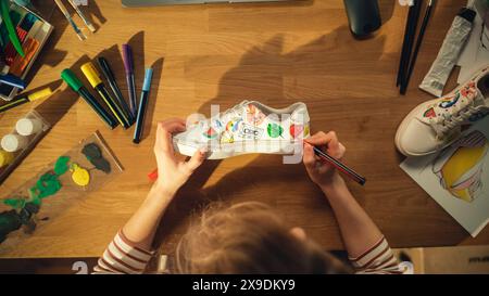 Top View of Female Designer Creating Hand Made Shoes, Drawing on Them at Home. Woman Working in Creative Mess on the Table. Footwear Customising and Creative Occupation Concept. Close Up. Stock Photo