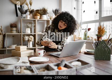 Charismatic woman seller in souvenir shop takes pictures of goods at phone. Stock Photo