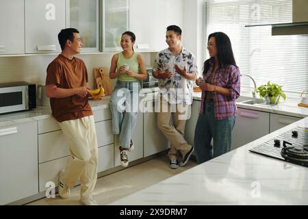 A group of friends engaging in a lively conversation and enjoying snacks in a spacious and well-lit kitchen Stock Photo