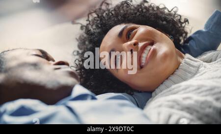 Young Happy Smiling Black Couple Is Laying on the Floor and Enjoying an Intimate Moment. Man Talk to his Wife, they are Dreaming About Bright Future Together. Casual Lifestyle Concept. Stock Photo