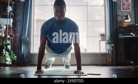 Athletic Black Man Doing Push Up Exercises and Using Mobile Smartphone as Timer. Authentic Male Doing Physical Workout, He is Training at Stylish Home with Minimalistic Interior. Stock Photo